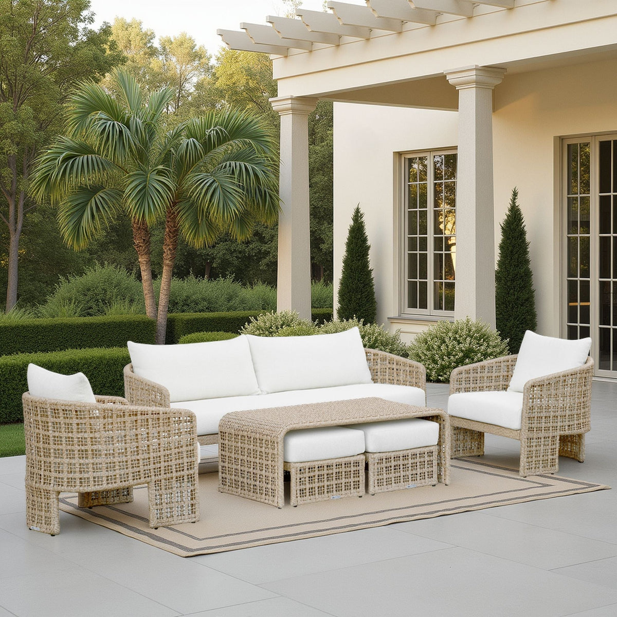 Outdoor patio set with wicker furniture and white cushions on a patio with a pergola and palm trees in the background.
